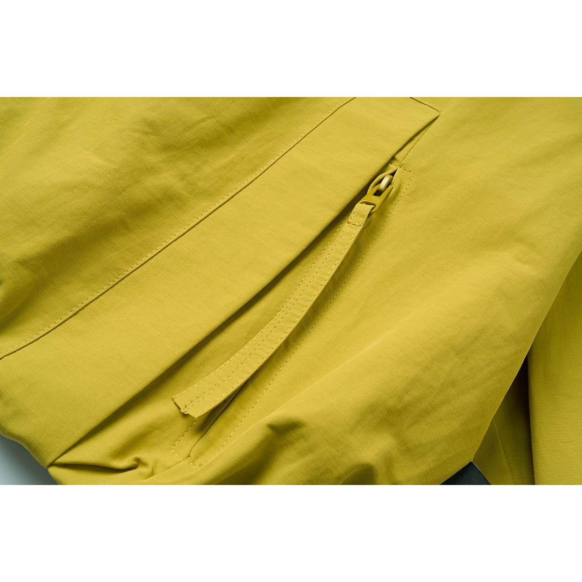 Close-up of the mustard yellow jacket's zipper and angled pocket opening.