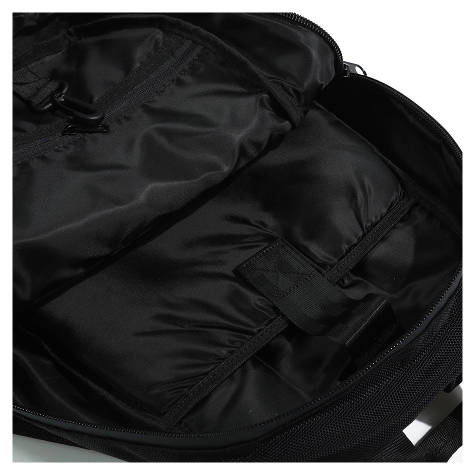 Close-up of an open black bag showing its zippered interior, stitched pocket, webbing strap and buckle.