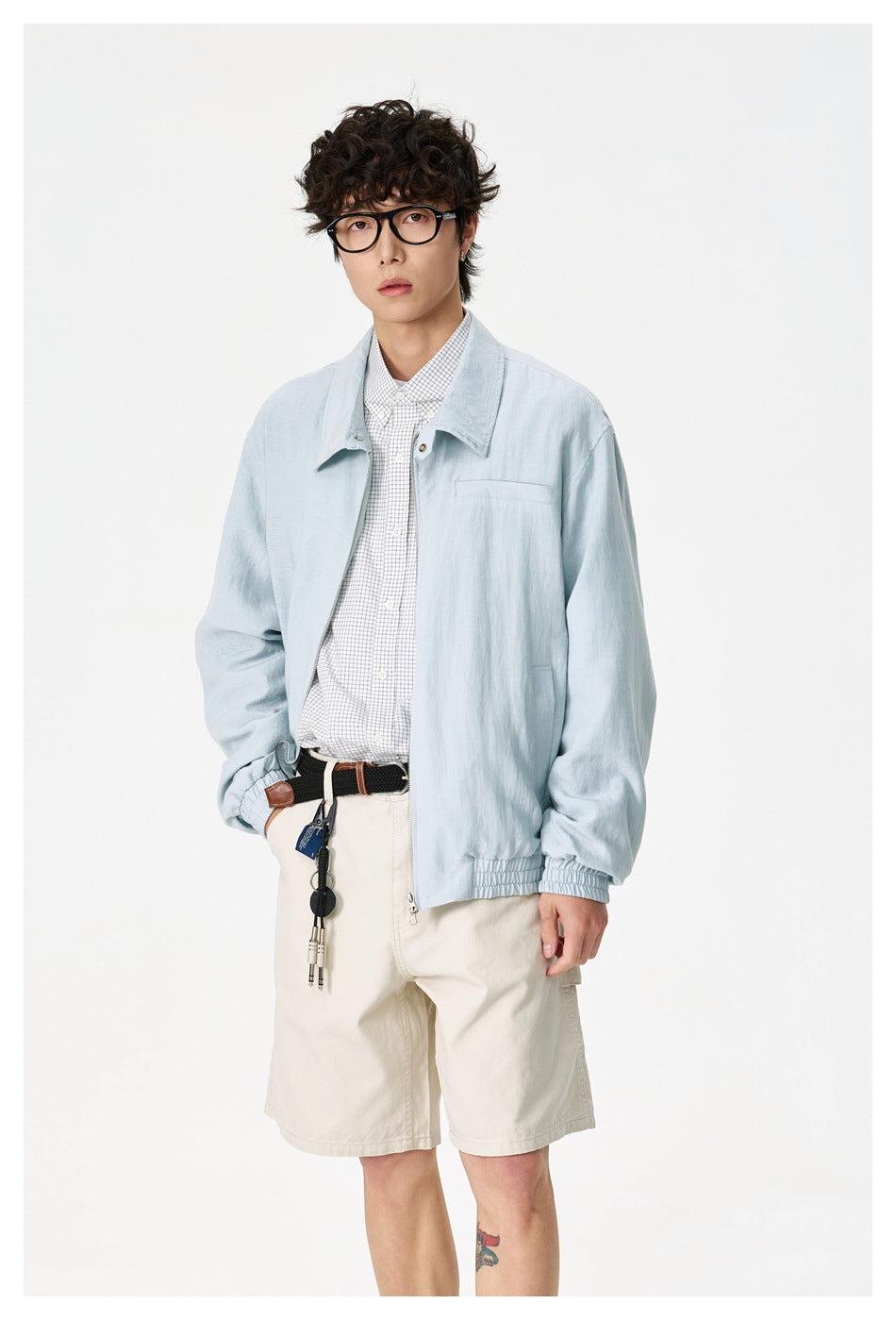 Closer view of a model wearing a pale blue zip-front jacket over a checked shirt and cream shorts.