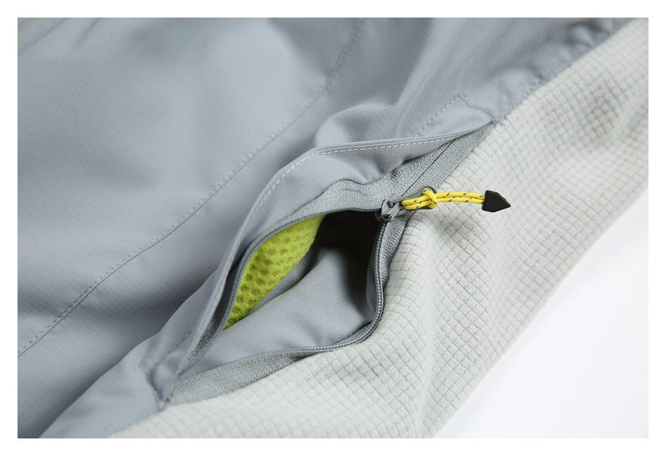 Close-up of an open gray jacket pocket with a yellow zipper pull, pale grid-textured panel, and neon yellow lining.