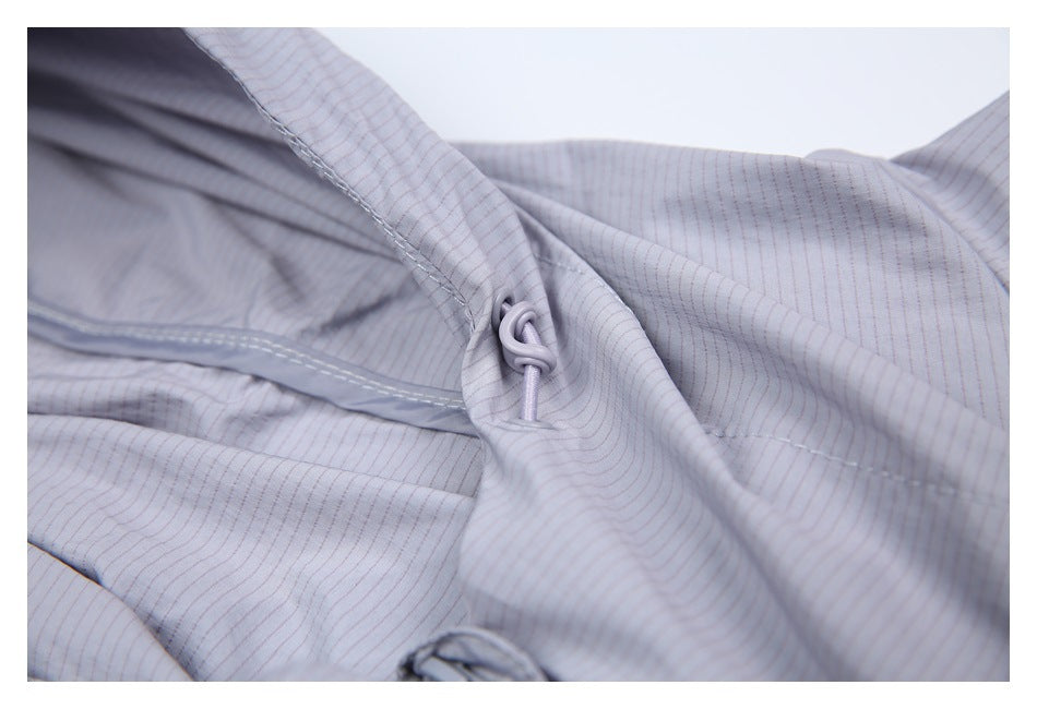 Close-up of a pale gray-lavender jacket's small drawcord and toggle beside a seam.