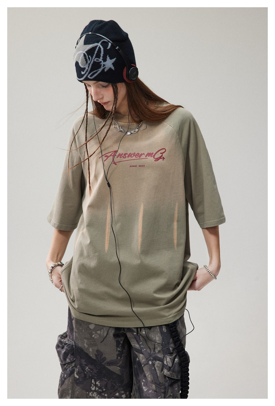 Model wearing an oversized sage-green T-shirt with burgundy chest lettering and pale streak graphics.