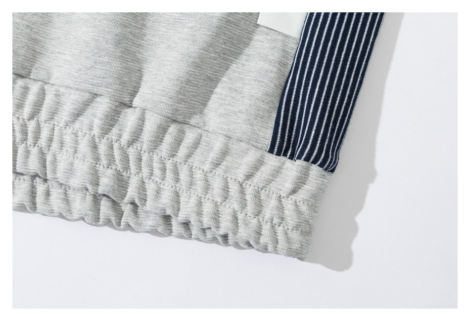 Close-up of the gathered elastic waistband and navy-and-white striped side panel on light gray joggers.