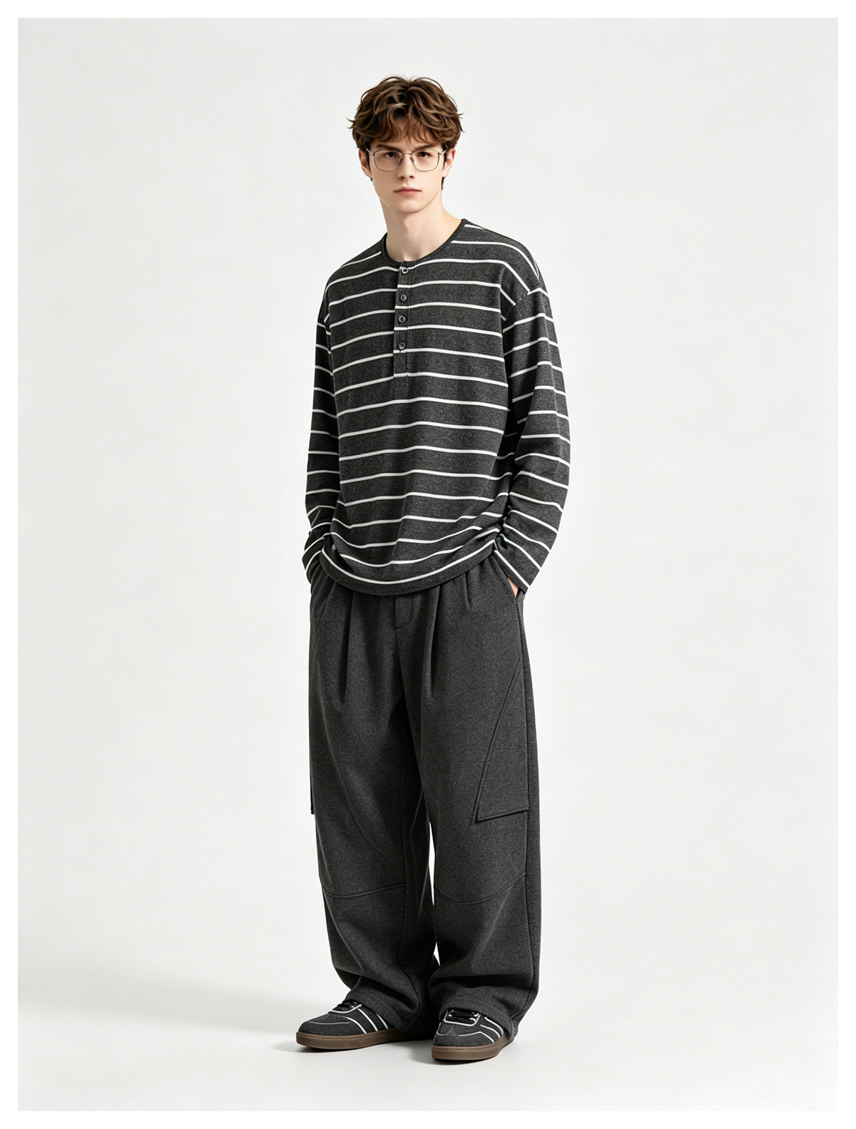 Model wearing a charcoal long-sleeve Henley with thin light horizontal stripes and loose dark trousers.
