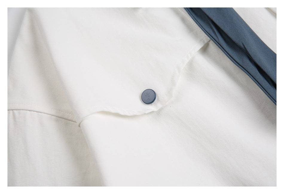 Close-up of a dark blue button on white garment fabric beside a slate-blue tie.