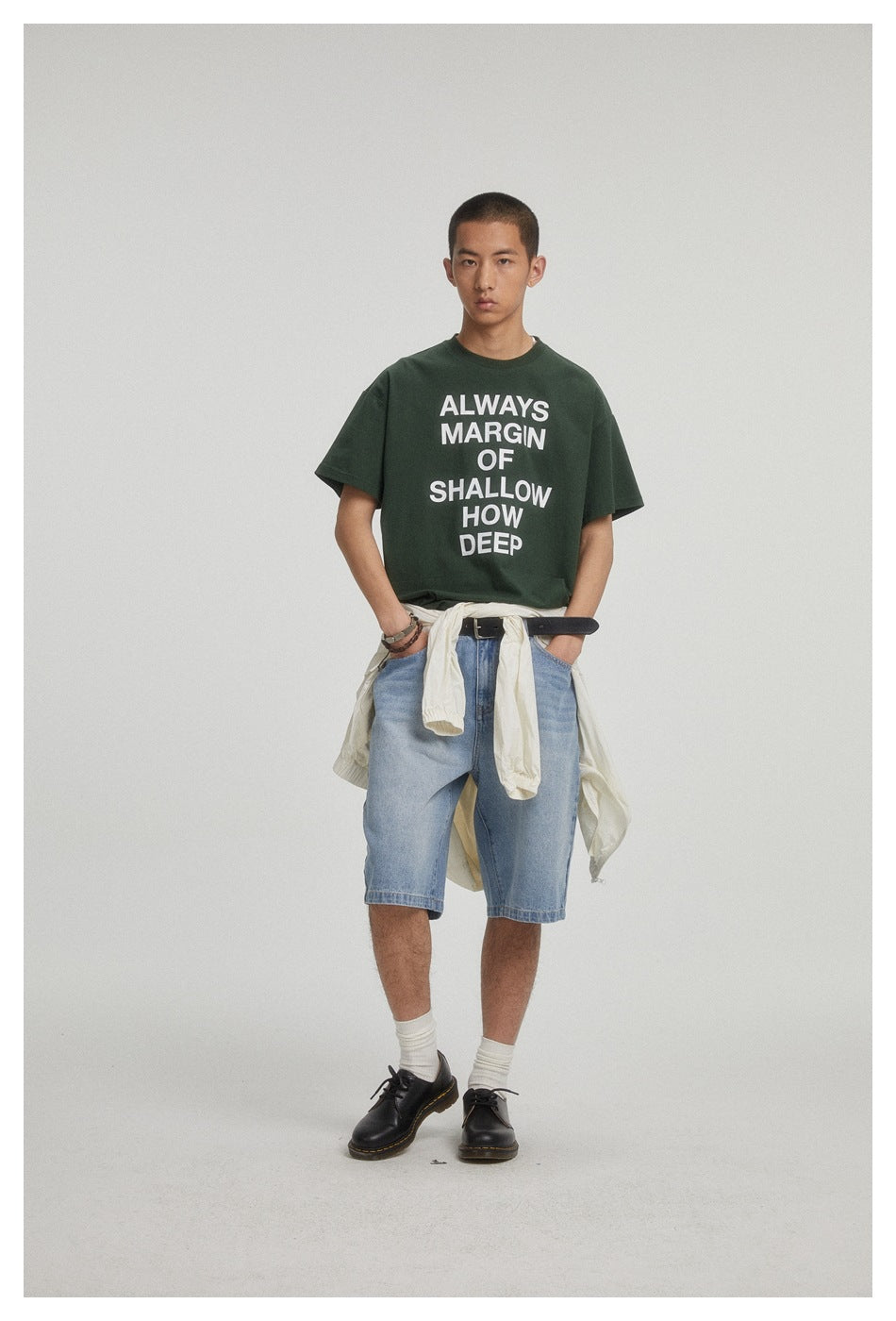 Front view of a model in a dark green text-print T-shirt and light blue denim shorts.