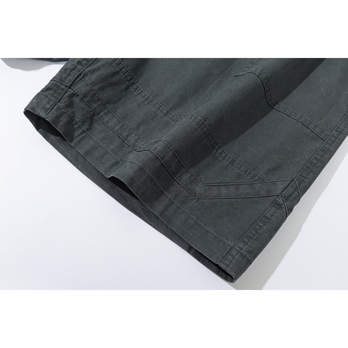 Close-up of charcoal shorts showing layered angular stitching along the hem.