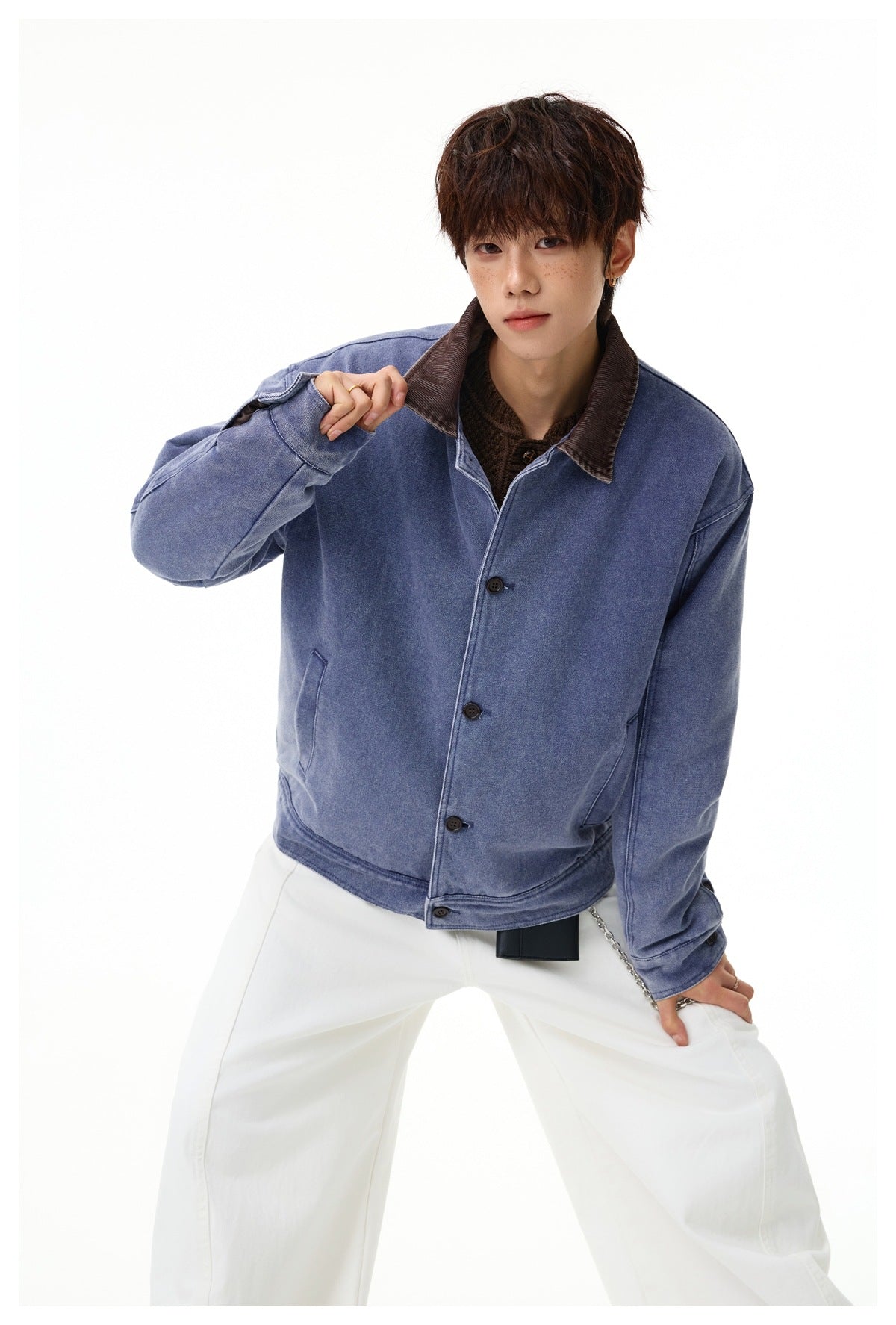 Model poses in a faded blue button-front jacket with a brown corduroy collar and white trousers.