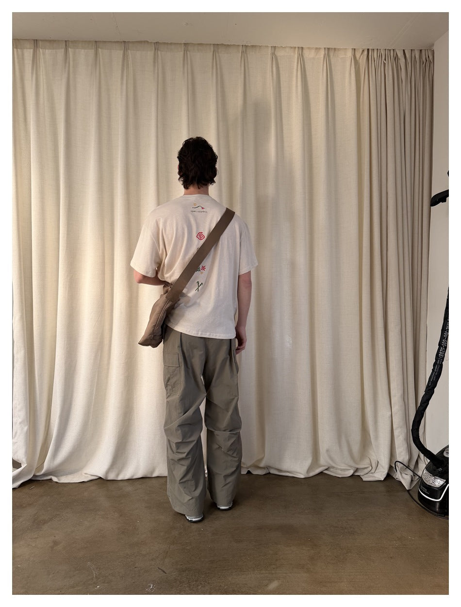 Back view of a man wearing loose gray-olive cargo pants and a cream graphic T-shirt.