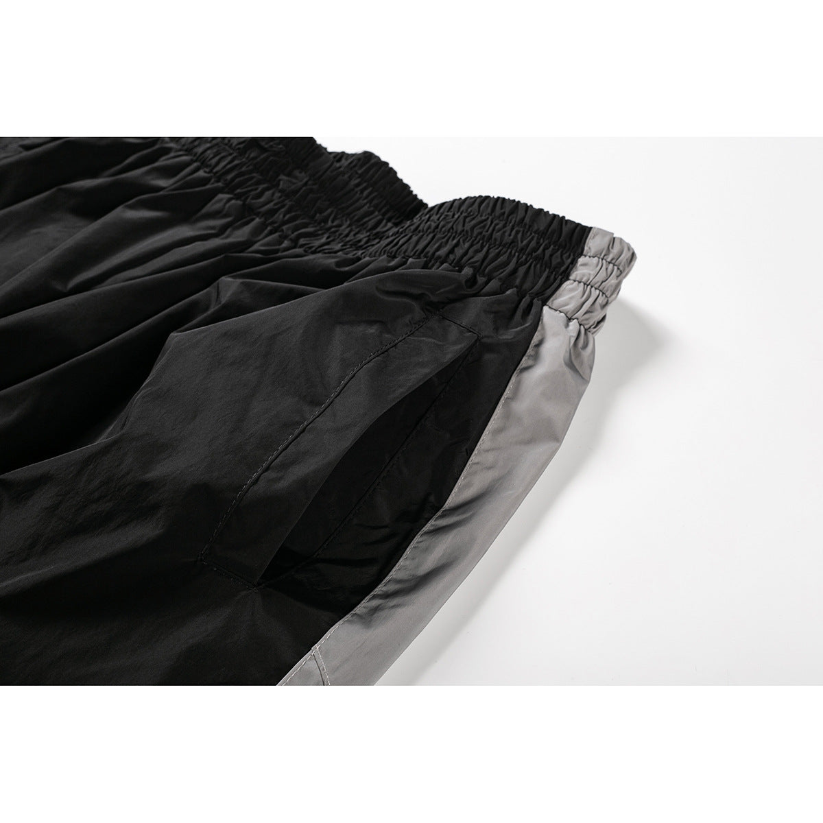Close-up of black shorts showing the gathered elastic waistband, a pocket, and gray side panel.