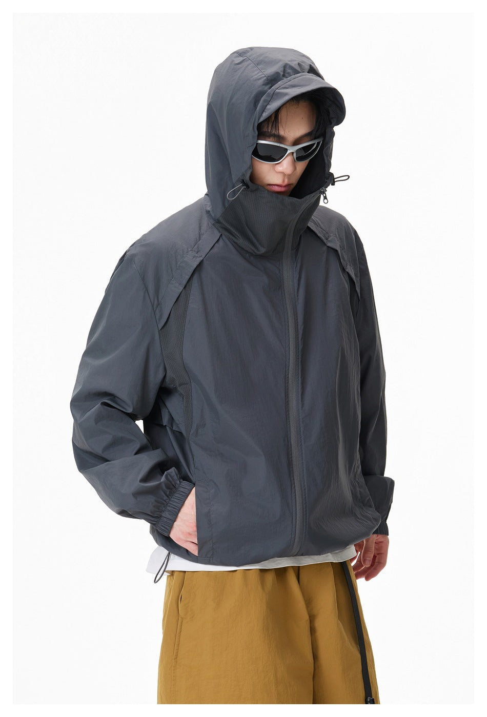 Model wearing a charcoal hooded jacket zipped high, with the hood up and hands in the pockets.