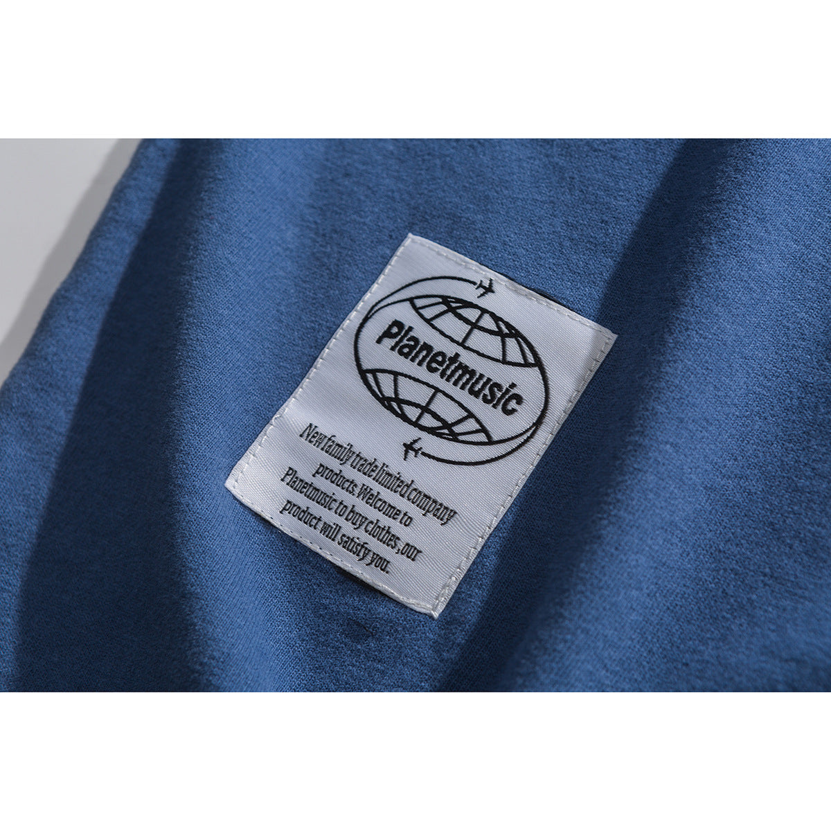 Close-up of a white Planetmusic label sewn onto blue T-shirt fabric.