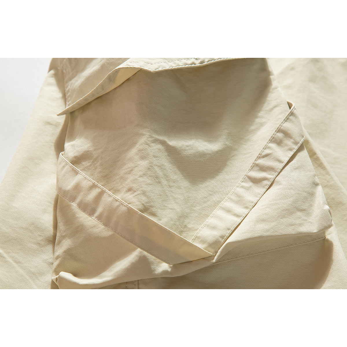 Close-up of a large stitched pocket on cream shorts.