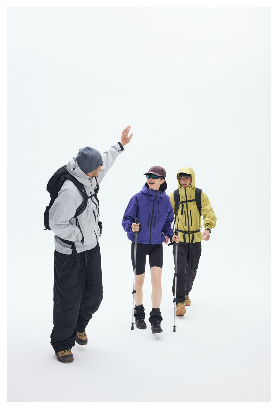 Three seated hikers wear gray, purple, and yellow hooded jackets with black hiking pants and backpacks.