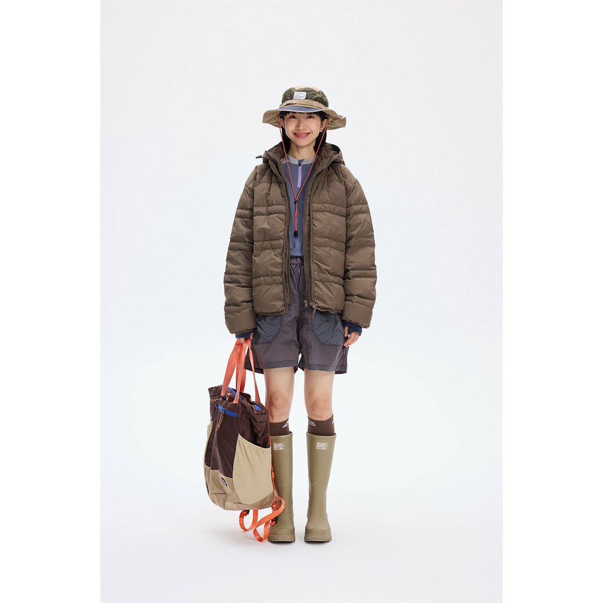 Model wearing a brown hooded quilted jacket with shorts and tall olive boots.