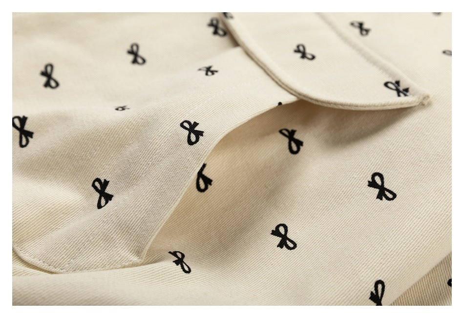 Close-up of beige fabric with black bow motifs and the edge of a folded collar.