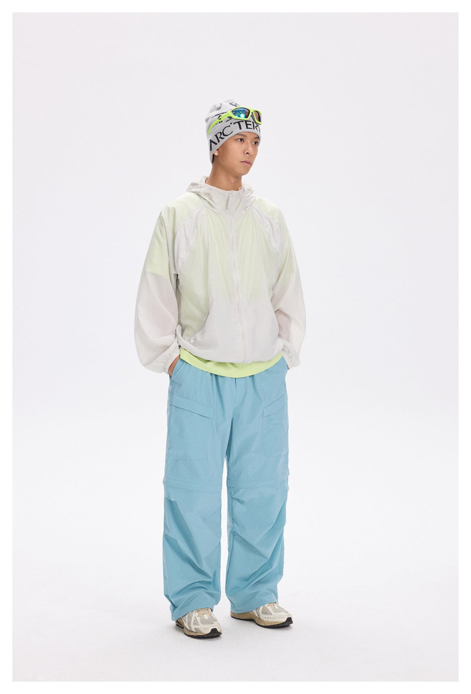 Man modeling a white and pale lime hooded zip jacket with loose light blue trousers.