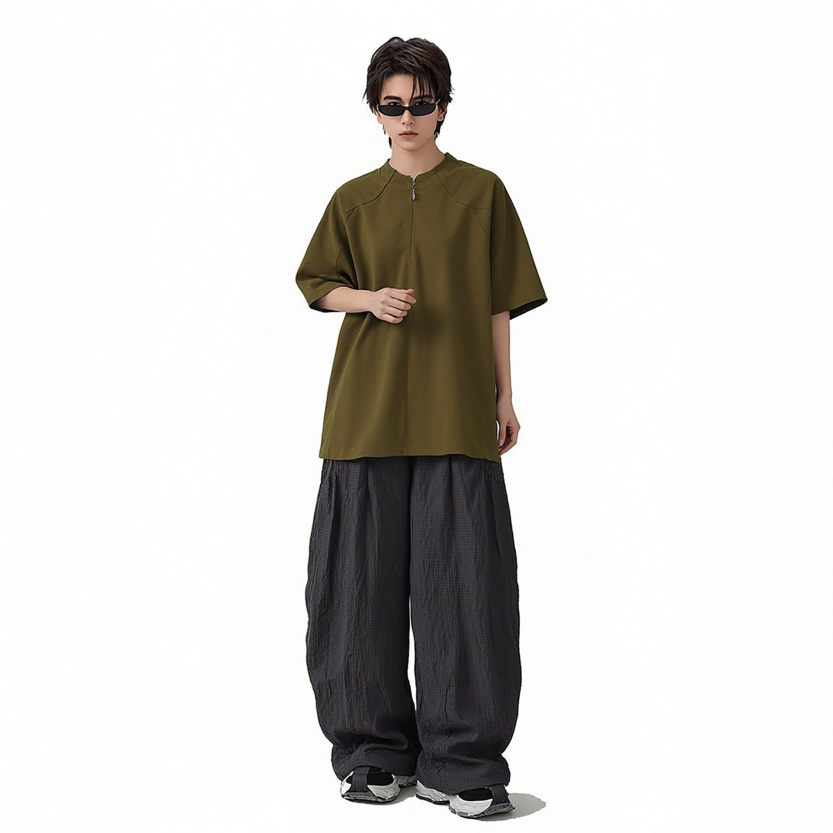 Model wearing an oversized olive short-sleeve zip-neck top with loose dark trousers.