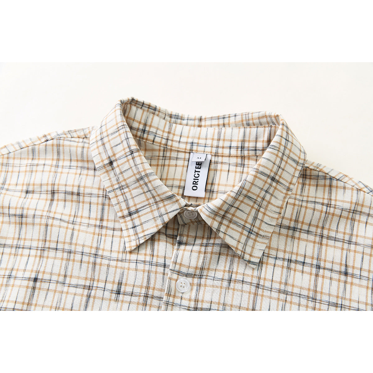 Close-up of a cream plaid button-up shirt collar and upper chest, with tan and dark gray lines.