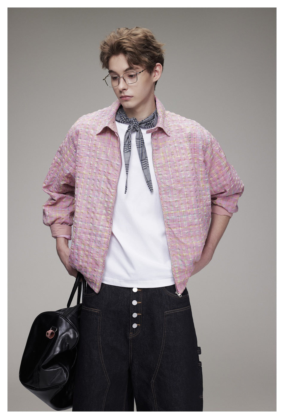 Model wearing a pink plaid zip jacket over a white shirt, with dark wide-leg pants and a gray neck scarf; front view.