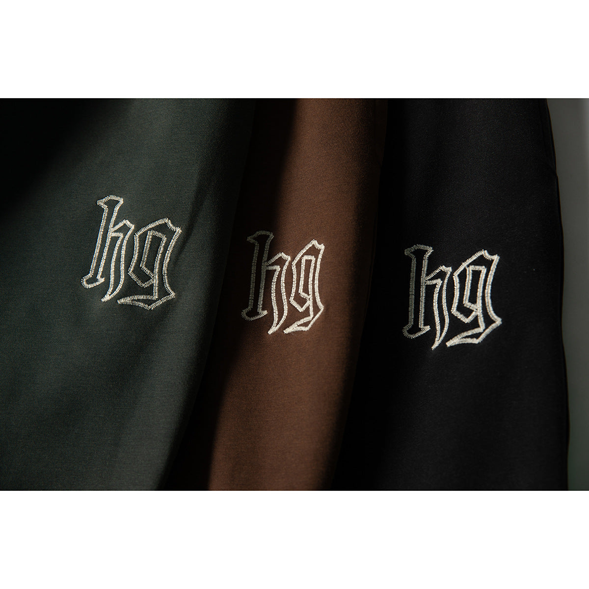 Close-up of matching embroidered motifs on dark green, brown, and black joggers.