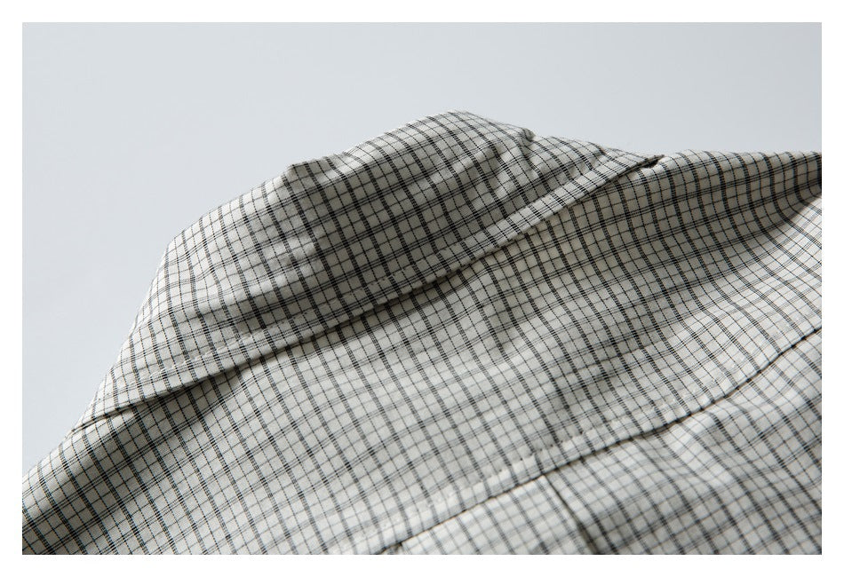 Close-up of off-white fabric with a fine black and gray plaid pattern and folded seams.