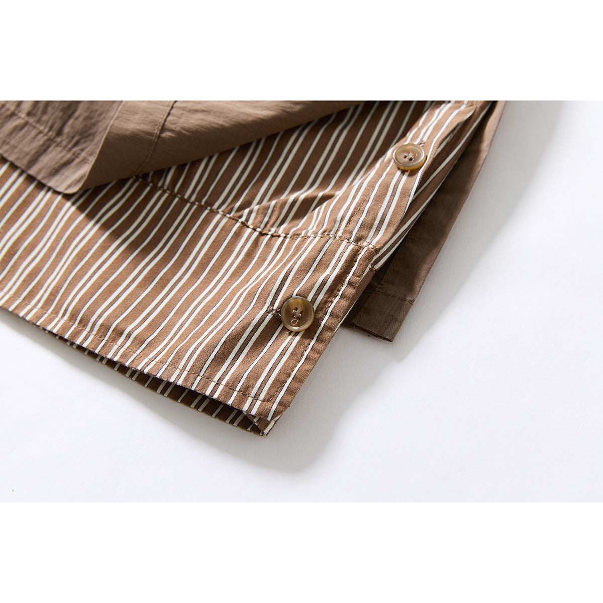 Close-up of taupe trousers with a striped inner panel, contrast buttons, and layered hem detail.