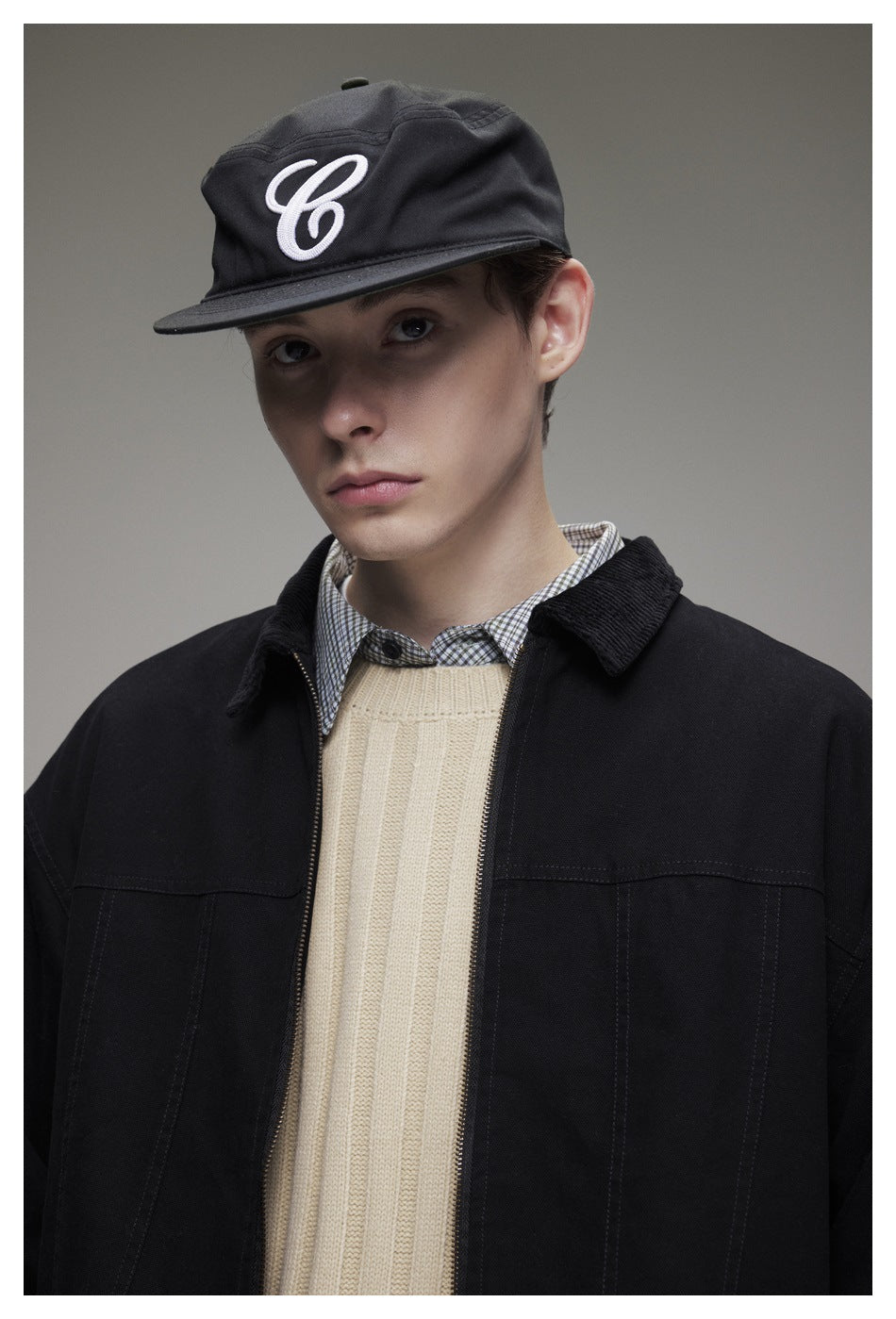 Close-up of a model wearing a black jacket over a cream ribbed sweater and checked shirt.