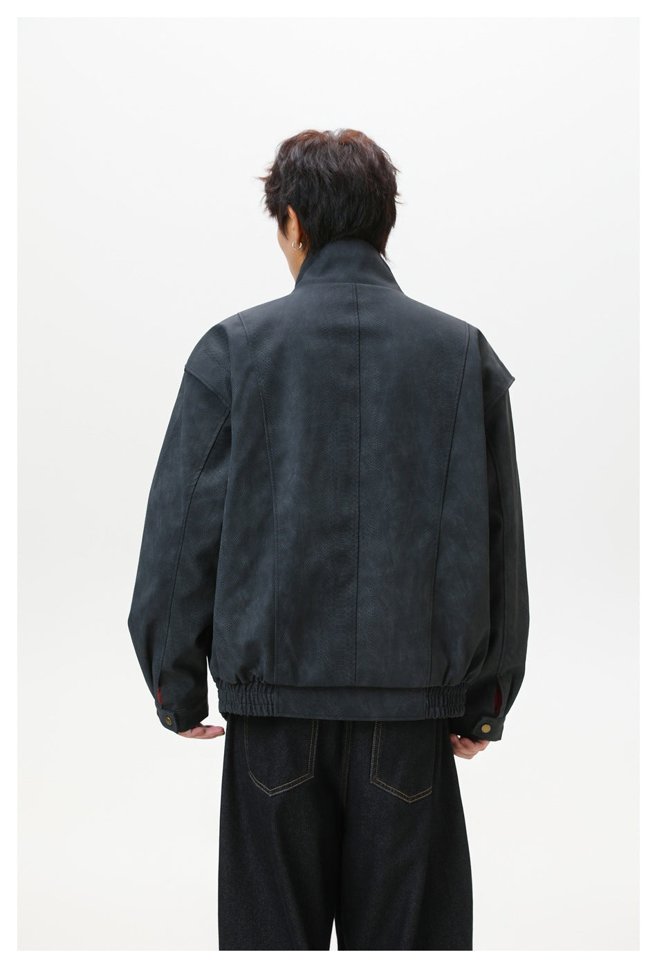 Back view of a model wearing a dark charcoal jacket with back seams, elastic hem and snap cuffs