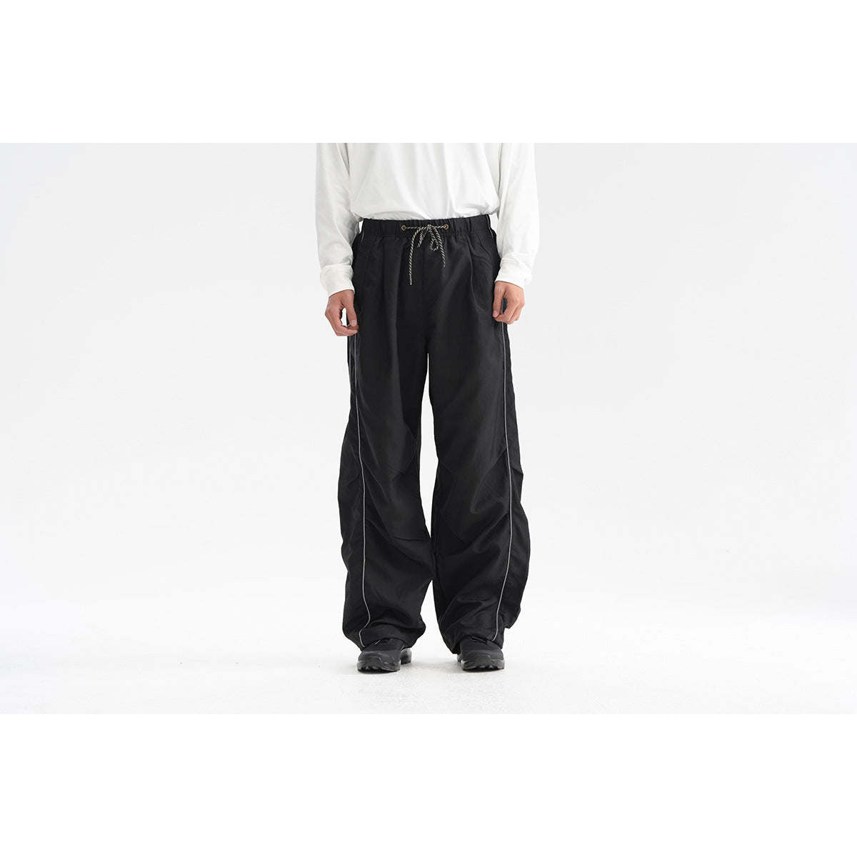Front view of a model wearing loose black drawstring pants with thin white side piping.