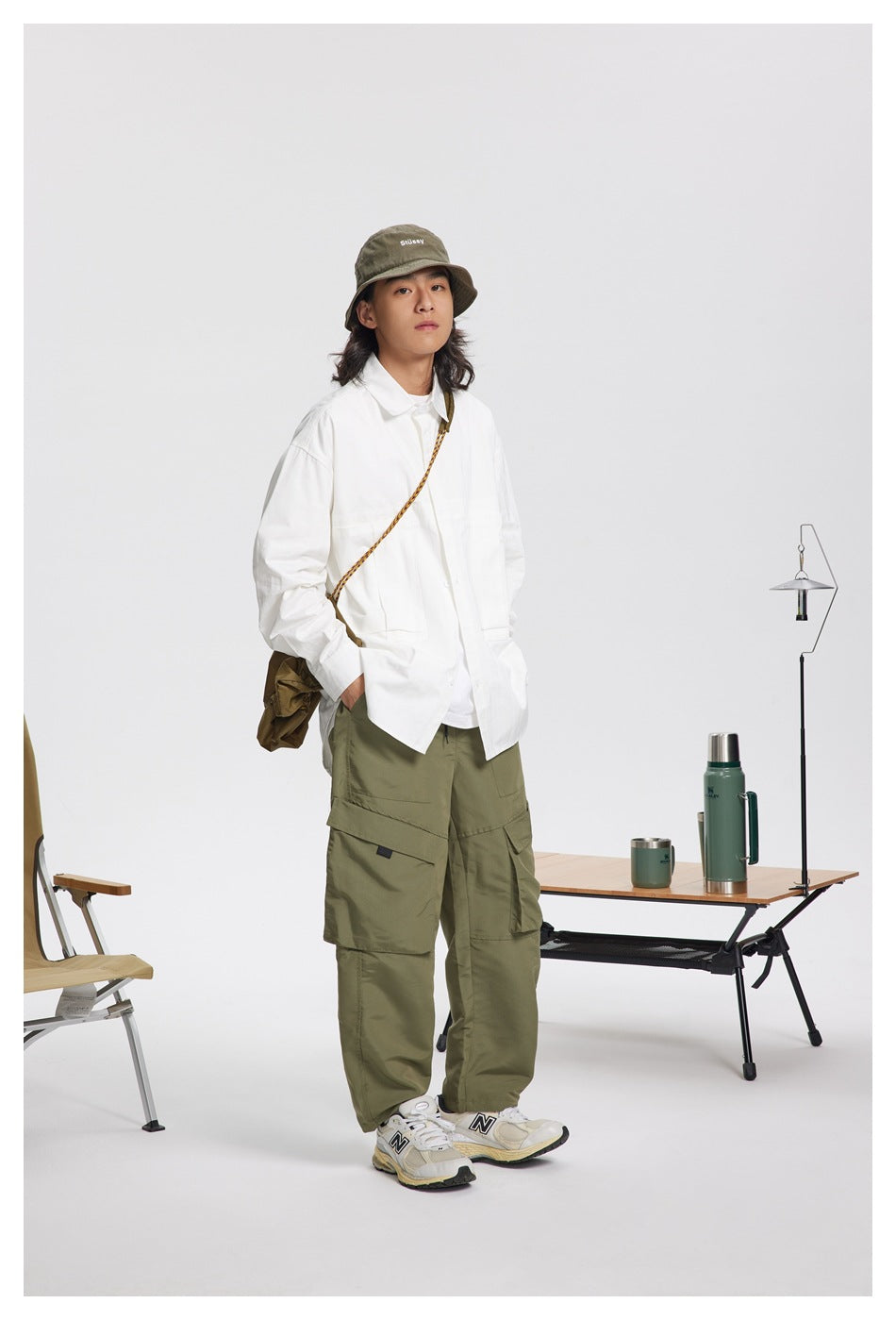 Model wearing a white oversized button-up shirt with chest pockets over olive cargo pants and a bucket hat