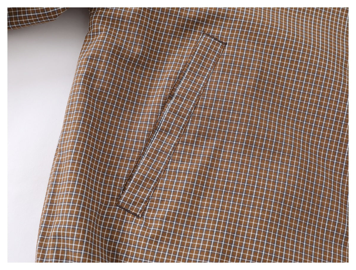Close-up of brown plaid fabric showing a narrow rectangular pocket with stitched edges.