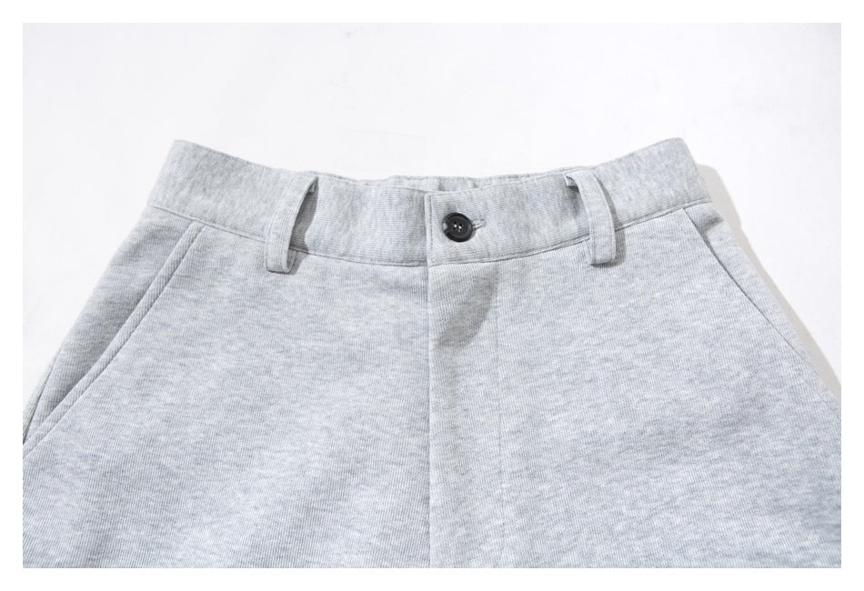 Close-up of the front waistband of light gray pants, showing a dark button, belt loops, and slanted pockets.
