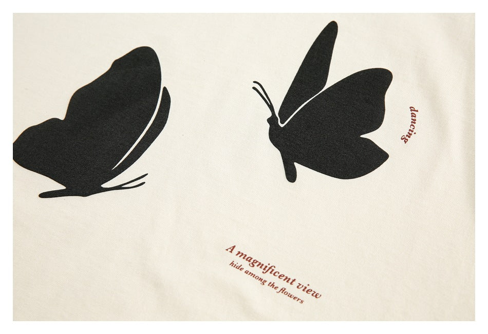 Close-up of two large black butterfly prints and brown English text on cream shirt fabric.