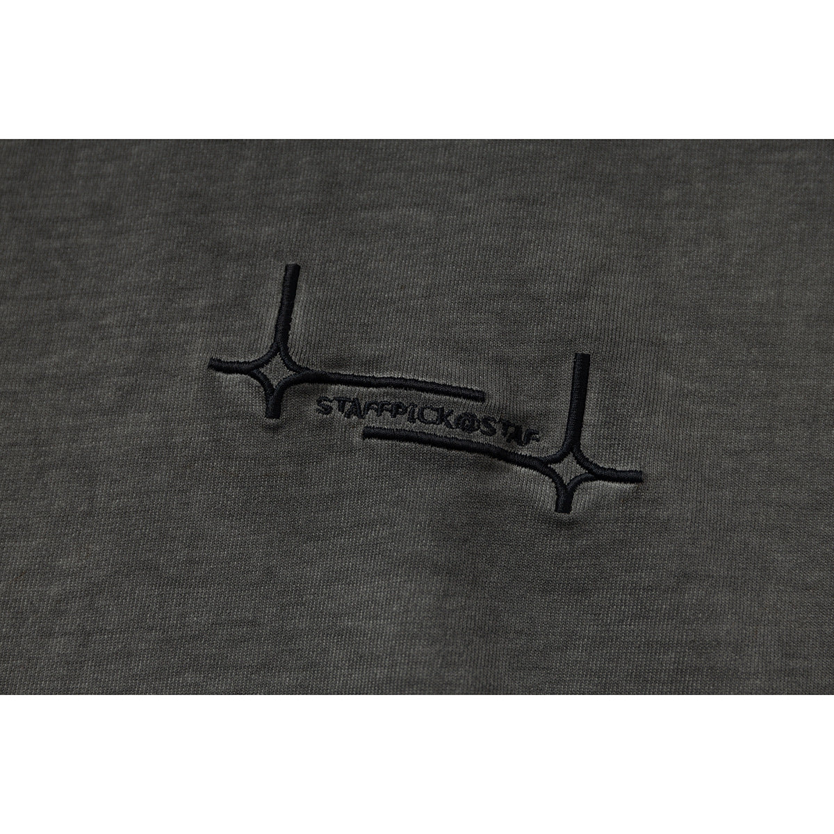Close-up of black embroidered lettering and an abstract line motif on washed charcoal fabric.