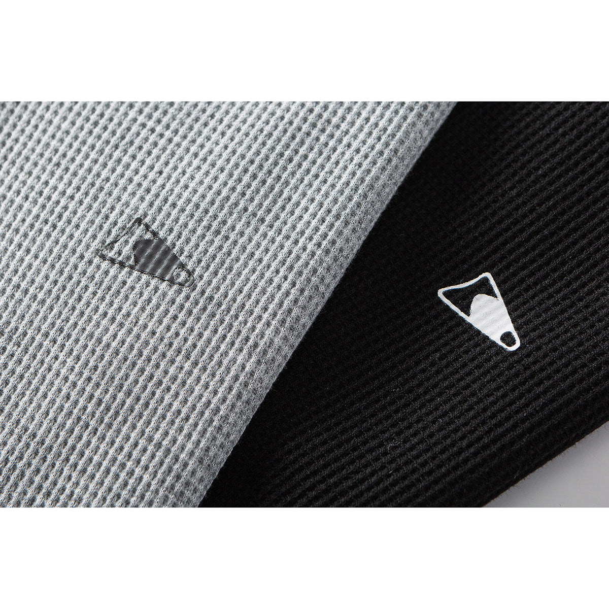 Close-up of gray and black textured polo fabric with small contrasting embroidered emblems.