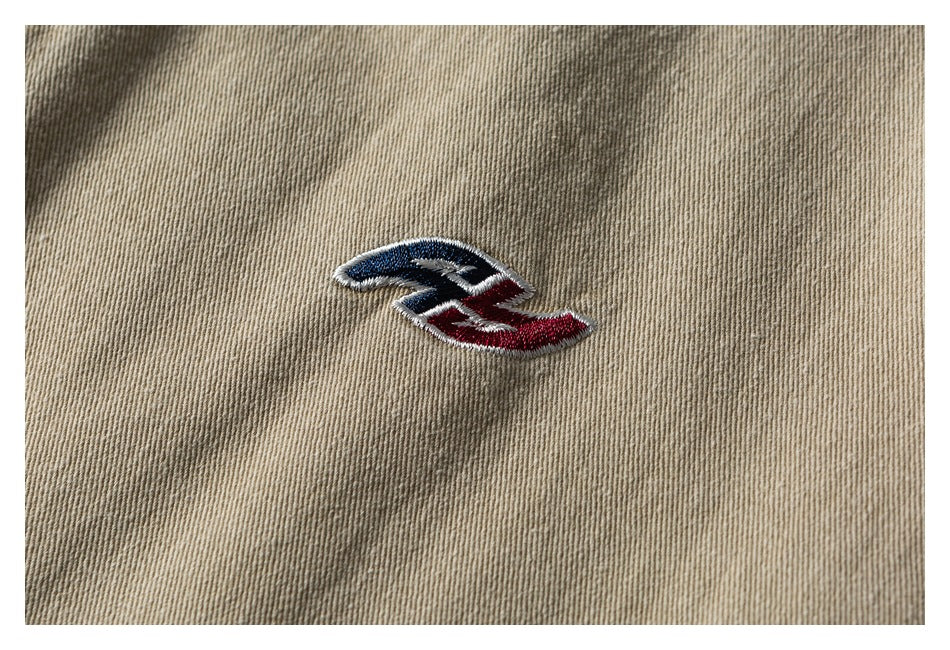 Close-up of a small red, navy, and white embroidered emblem on beige twill fabric.
