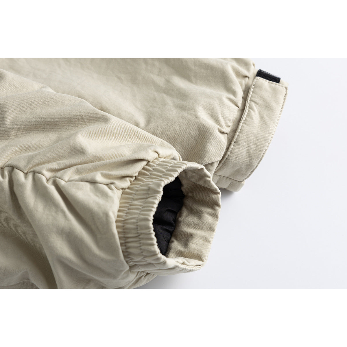 Close-up of a light beige jacket sleeve, showing its elastic cuff and adjustable tab.