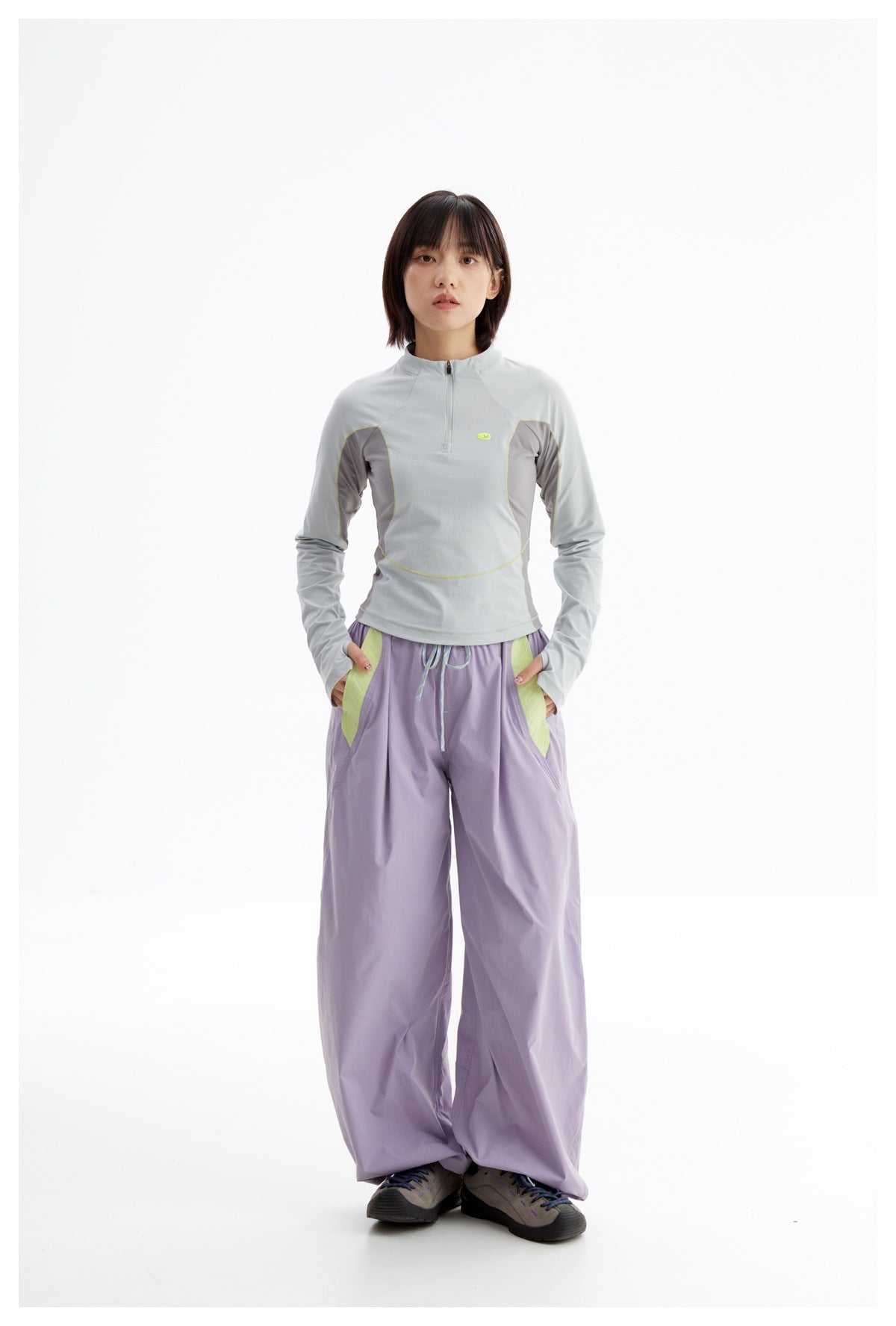 Model wearing a pale blue-gray quarter-zip top with lime piping and lavender wide-leg pants with lime accents.