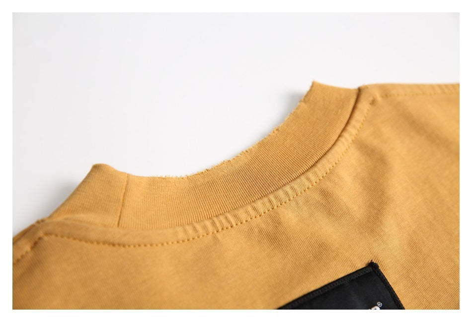 Close-up of the ochre T-shirt ribbed neckline, stitching, and partial black chest patch.