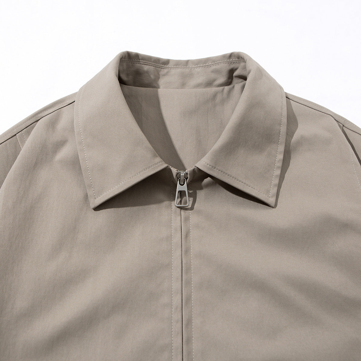 Close-up of a taupe jacket's pointed collar and centered metal zipper on a white background.