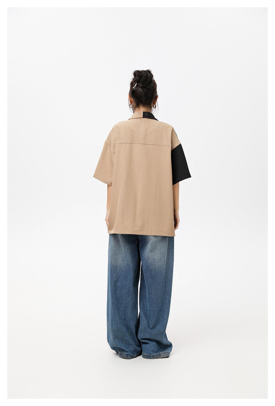 Back view of a model wearing the oversized tan shirt with black sleeve and collar accents, paired with wide-leg jeans.