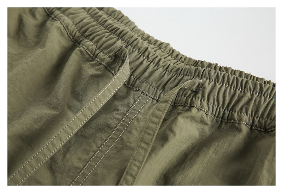 Close-up of olive shorts showing the gathered elastic waistband, drawstring and stitched seams.