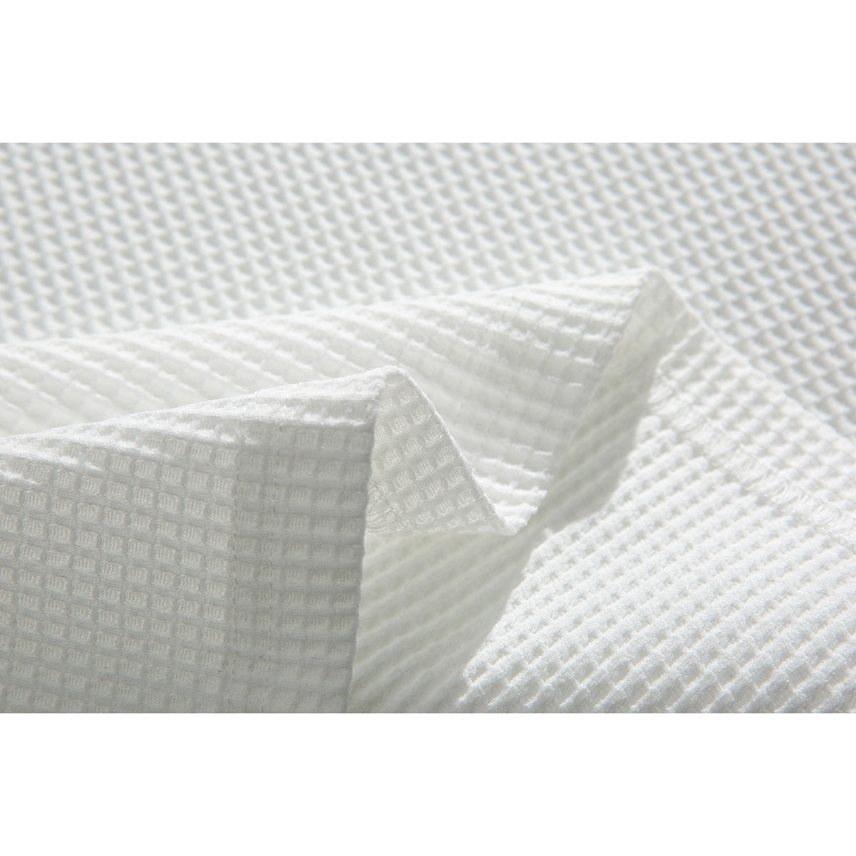 Close-up of folded white textured fabric showing the raised waffle pattern and stitched edge.