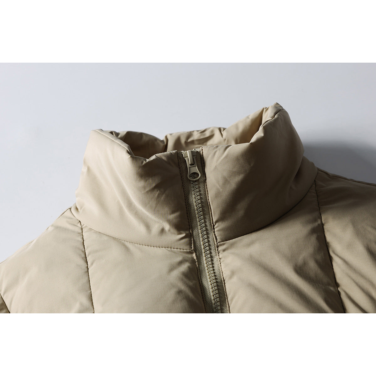 Close-up of a taupe puffer jacket's tall padded collar and front zipper.