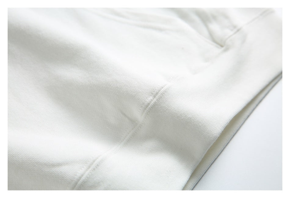 Close-up of the white hoodie’s fabric and a curved seam near the pocket.
