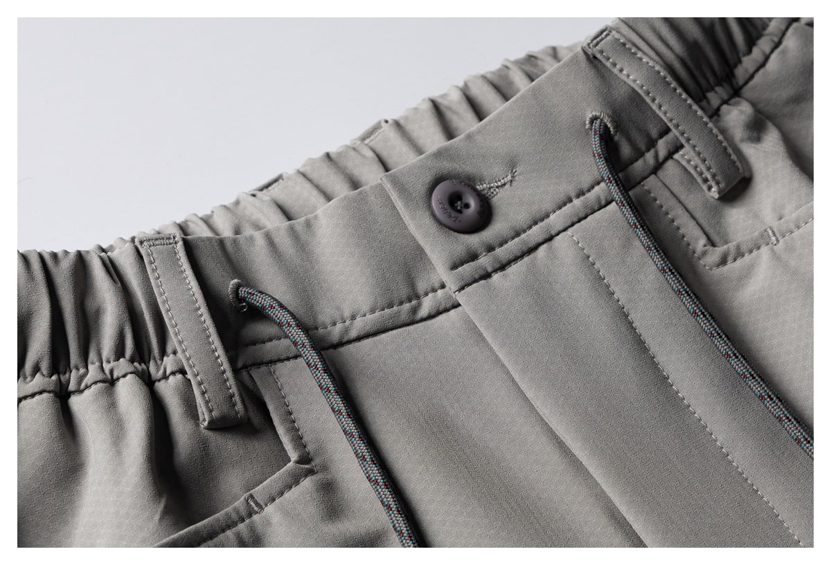 Close-up of gray shorts showing the elastic waistband, button closure, belt loop, and multicolored drawcords.