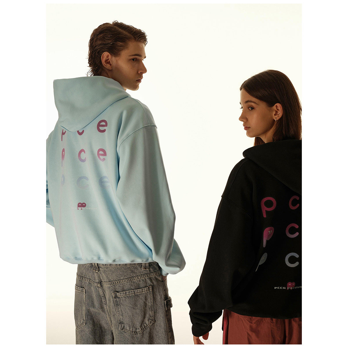 Two models look back wearing light blue and black hoodies with colorful lettering across the backs.