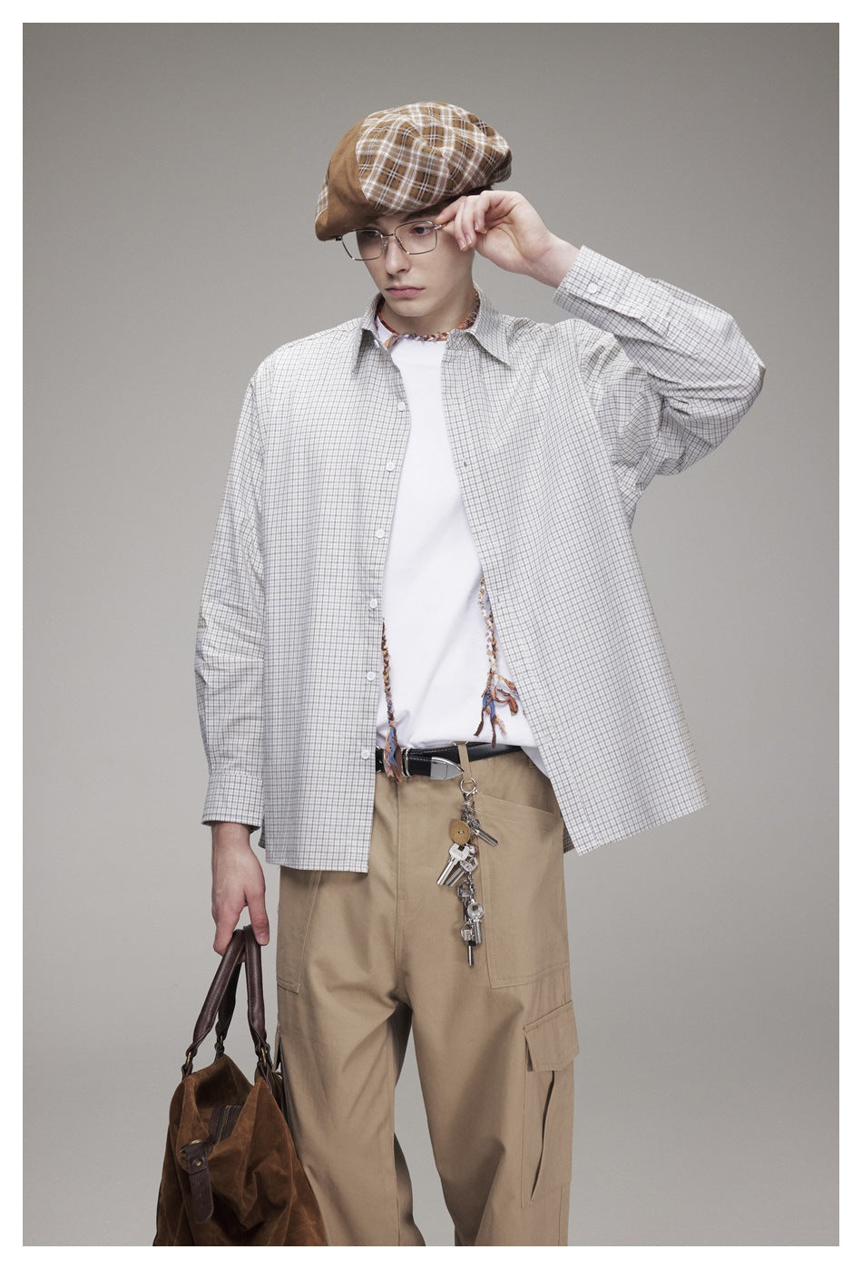 Model wearing an open check button-up shirt over a white tee with khaki cargo pants, holding a brown bag