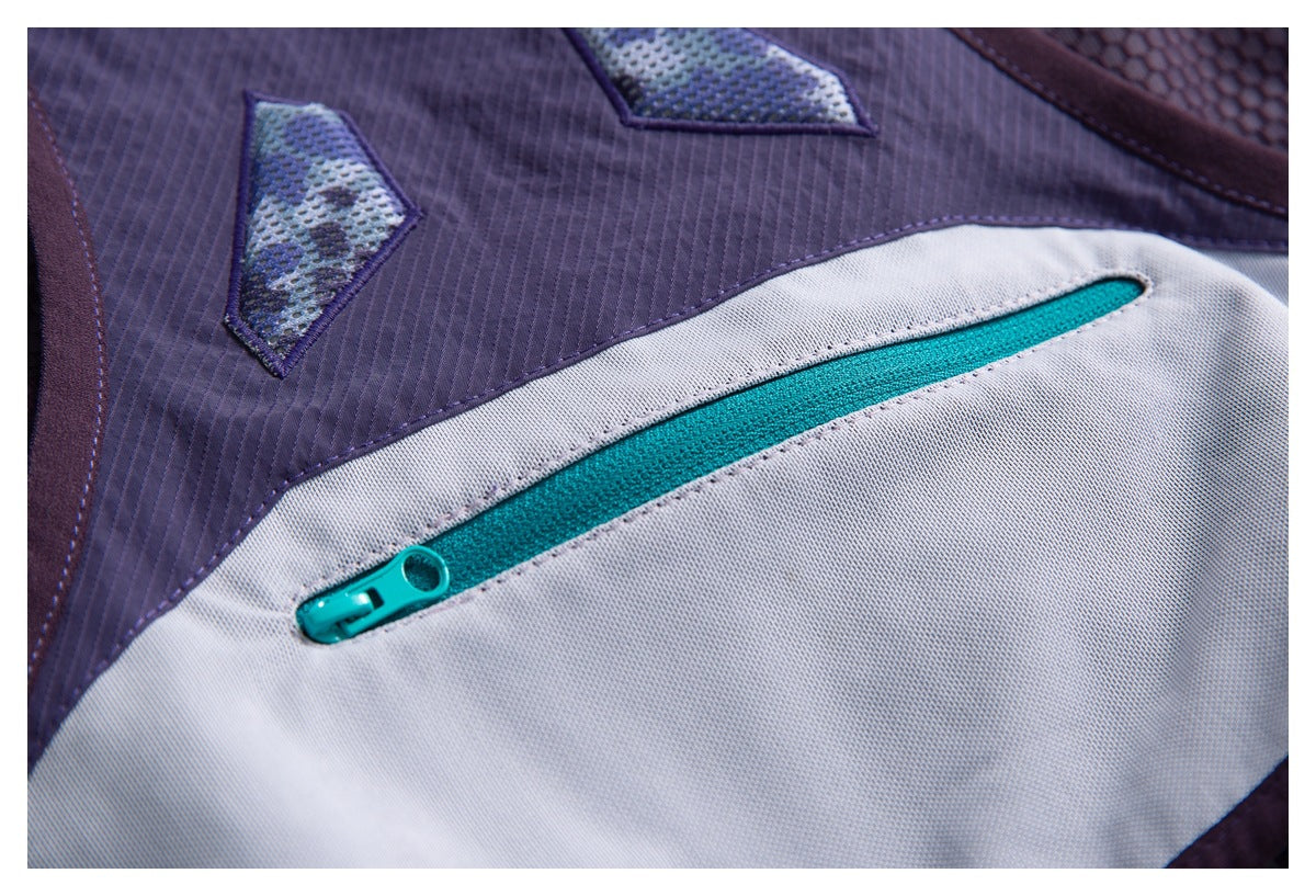 Close-up of a turquoise zipper across a light gray panel with dark purple trim and patterned fabric.